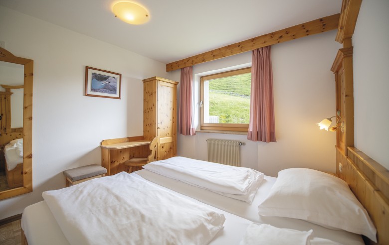 La foto mostra la camera in legno di cedro con vista sulla natura. Si vede uno specchio, una scrivania, un armadio e un letto matrimoniale.