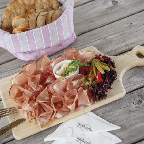 Rifugio Molignon Alpe di Siusi | Il fascino dei rifugi per il palato: Gustate la nostra deliziosa dieta dei rifugi L'immagine mostra una foglia di pancetta con cetriolo aceto e spalmato. Sullo sfondo si vede un cestino del pane.