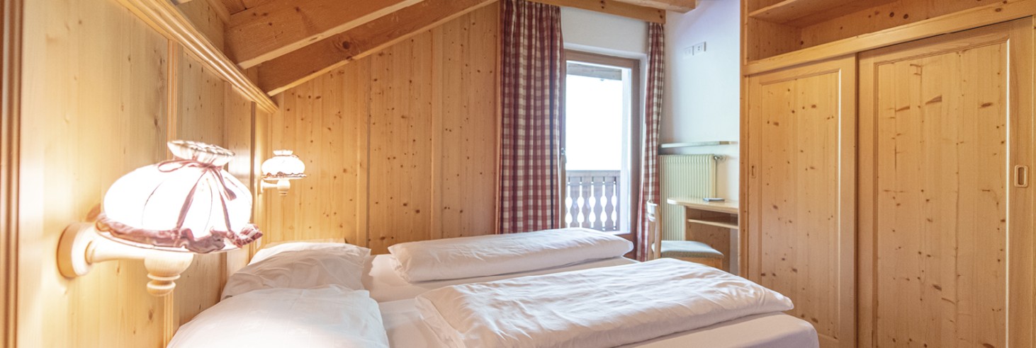 Rifugio Molignon Alpe di Siusi | Unico in Alto Adige: Alpe di Siusi con scivoli e piatti La foto mostra il letto matrimoniale, un armadio e il balcone con vista sulle Dolomiti circostanti.