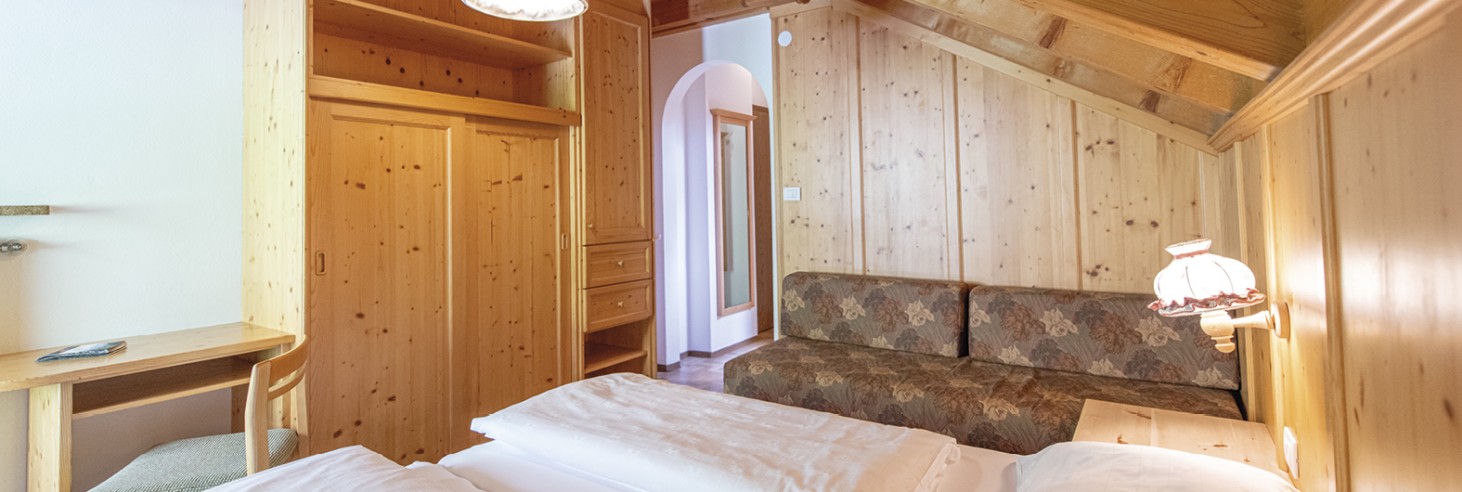 Rifugio Molignon Alpe di Siusi | L'Alpe di Siusi in Alto Adige: dormire nella natura La foto mostra una camera matrimoniale con un divano, un armadio e una scrivania. La camera è decorata con un sacco di legno.