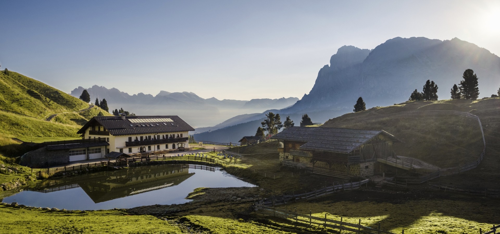 Das Bild zeigt die Molignonhütte mit dem See mit Blick richtung Land- und Plattkofel auf der Seiser Alm.