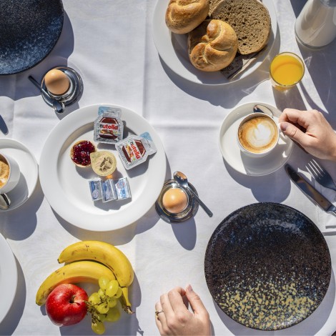 La foto mostra un tavolo per la colazione apparecchiato. Ci sono piatti da guardare, così come frutta, pane, varie spalmature e anche caffè.