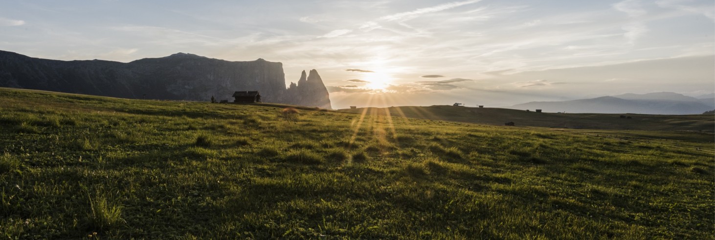 Das Bild zeigt den Schlern auf der Seiser Alm. Die Sonne geht dahinter auf.